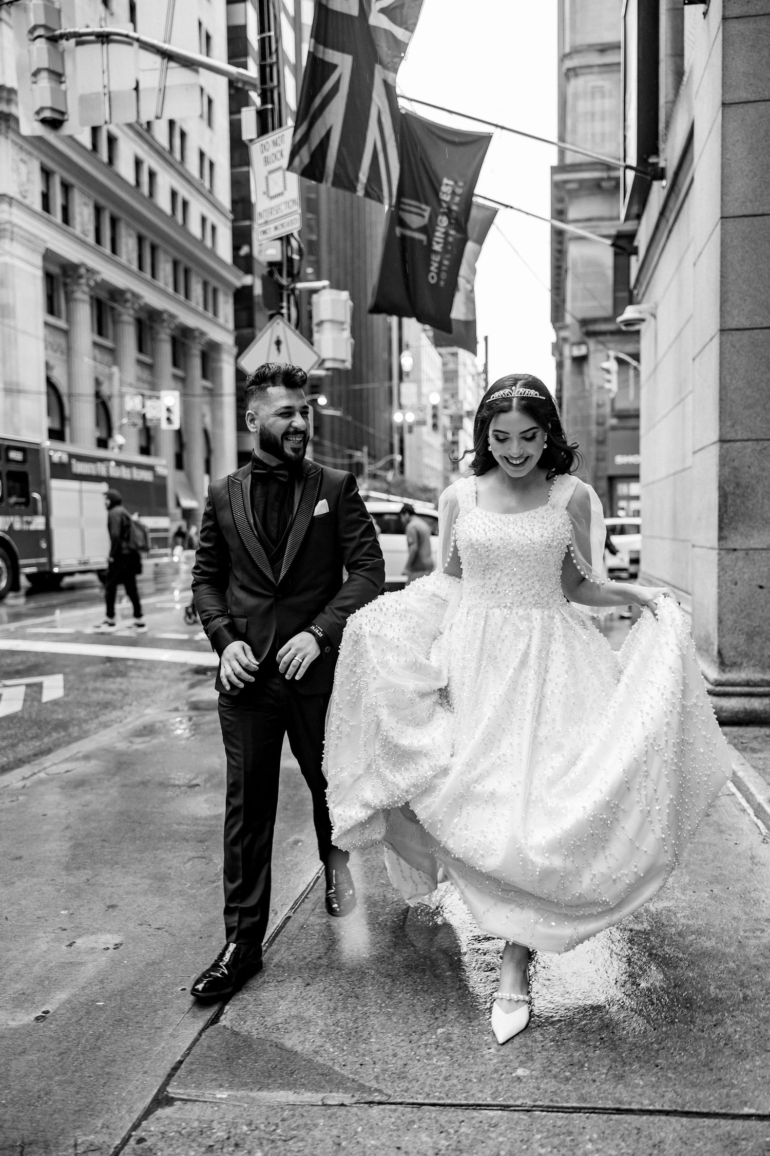Black and white urban wedding photos on city sidewalk with playful poses.