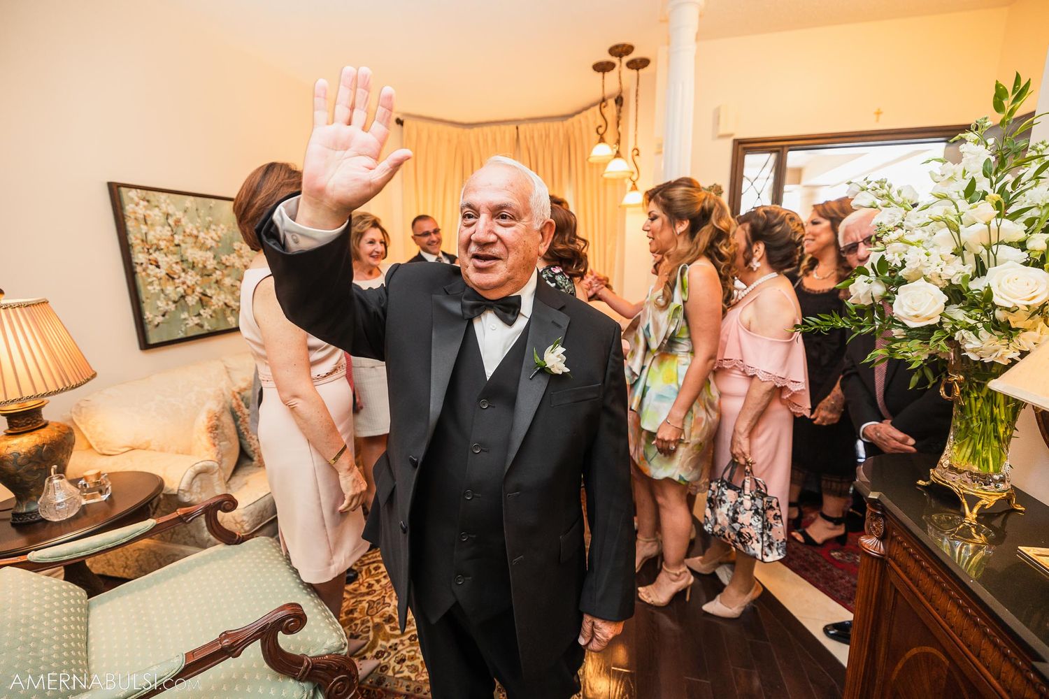 Man in black tuxedo waves to camera during wedding celebration.