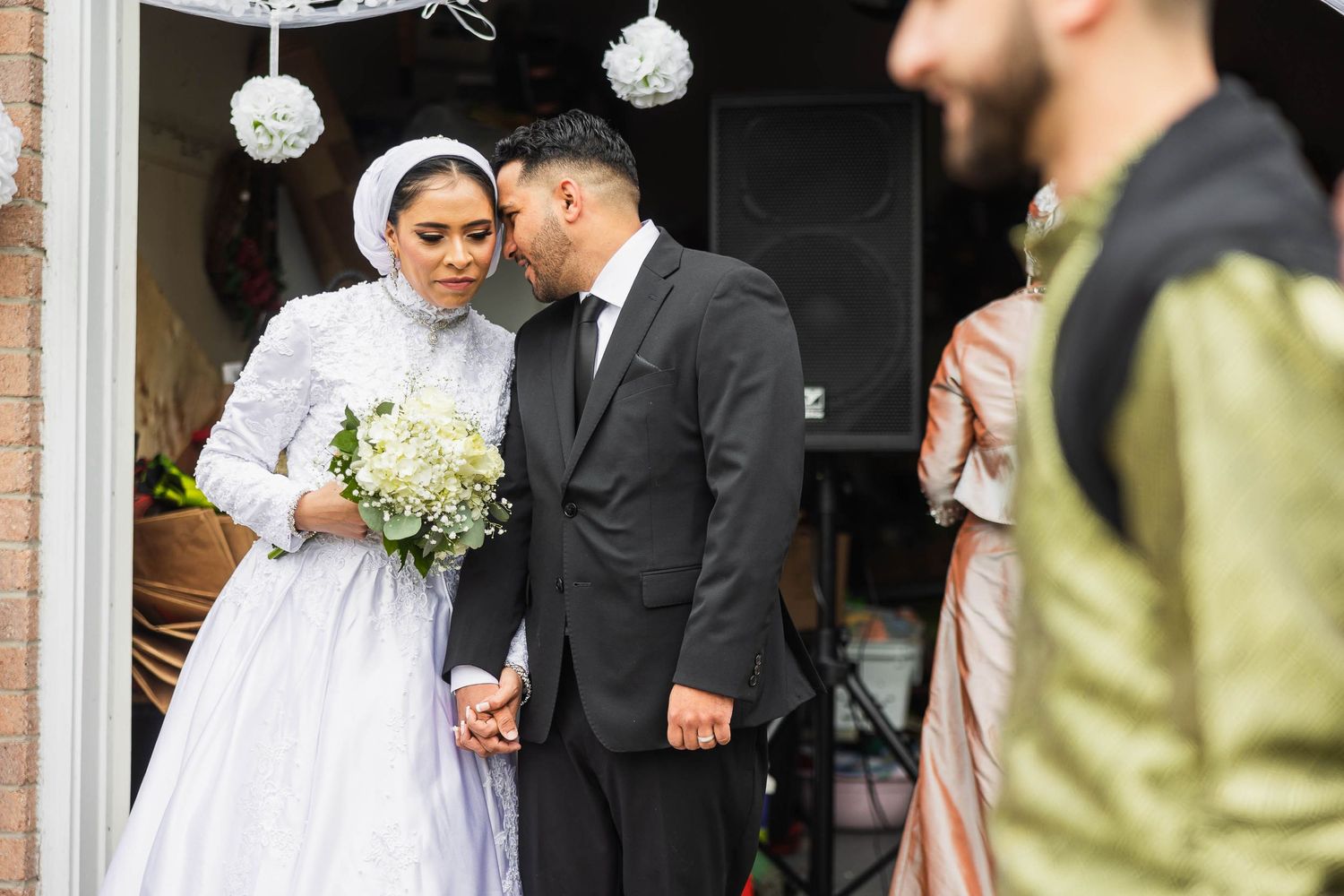 A newlywed couple stands under decorative white lanterns at their wedding venue entrance.