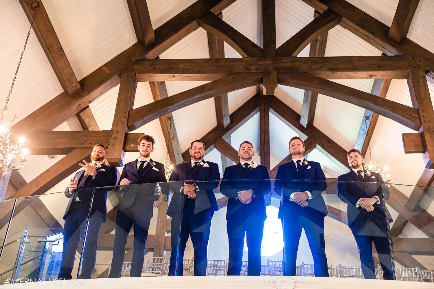 Groomsmen pose together under rustic wooden beams in a chapel during a wedding ceremony.