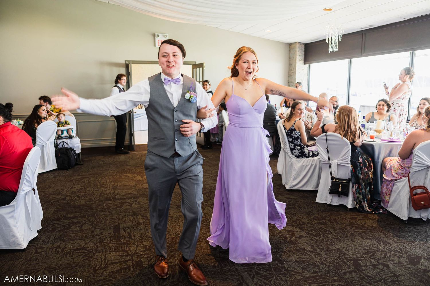 Wedding party members dance energetically during reception in venue with brown carpeting.