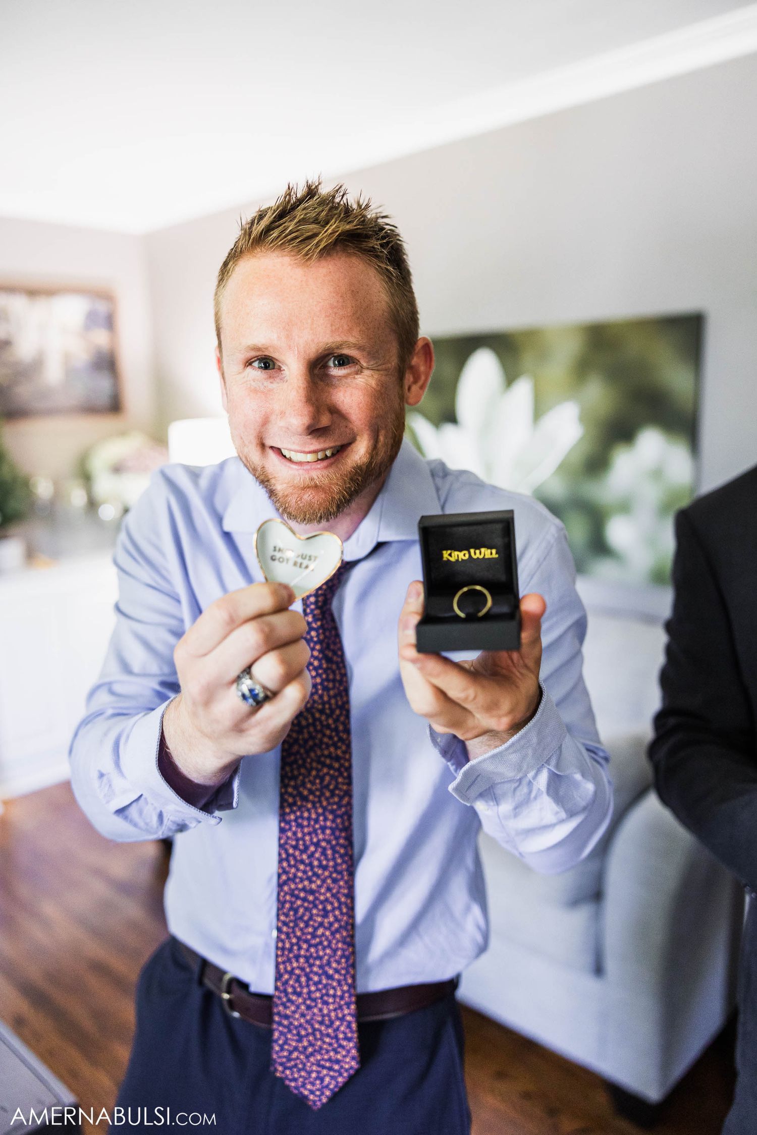 Person in dress shirt and tie holding small ring box while getting ready for wedding.
