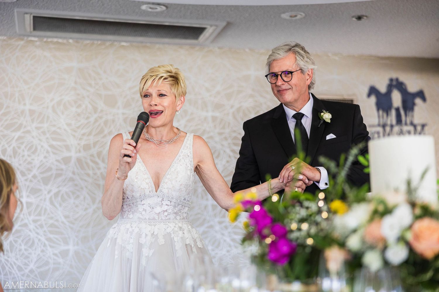 Wedding speeches being delivered in an elegant reception room with decorative wall patterns.