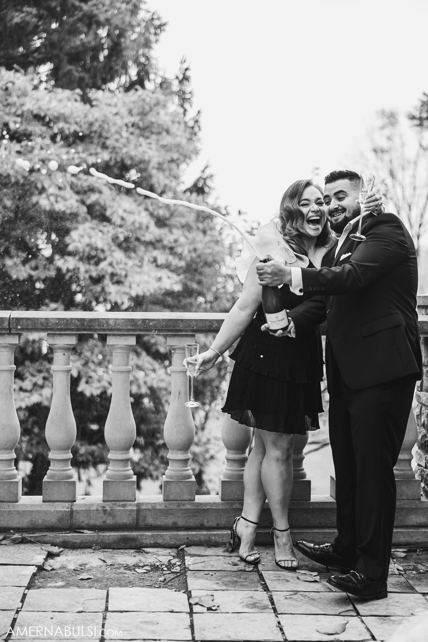 A couple enjoying champagne and laughter together on a stone terrace.