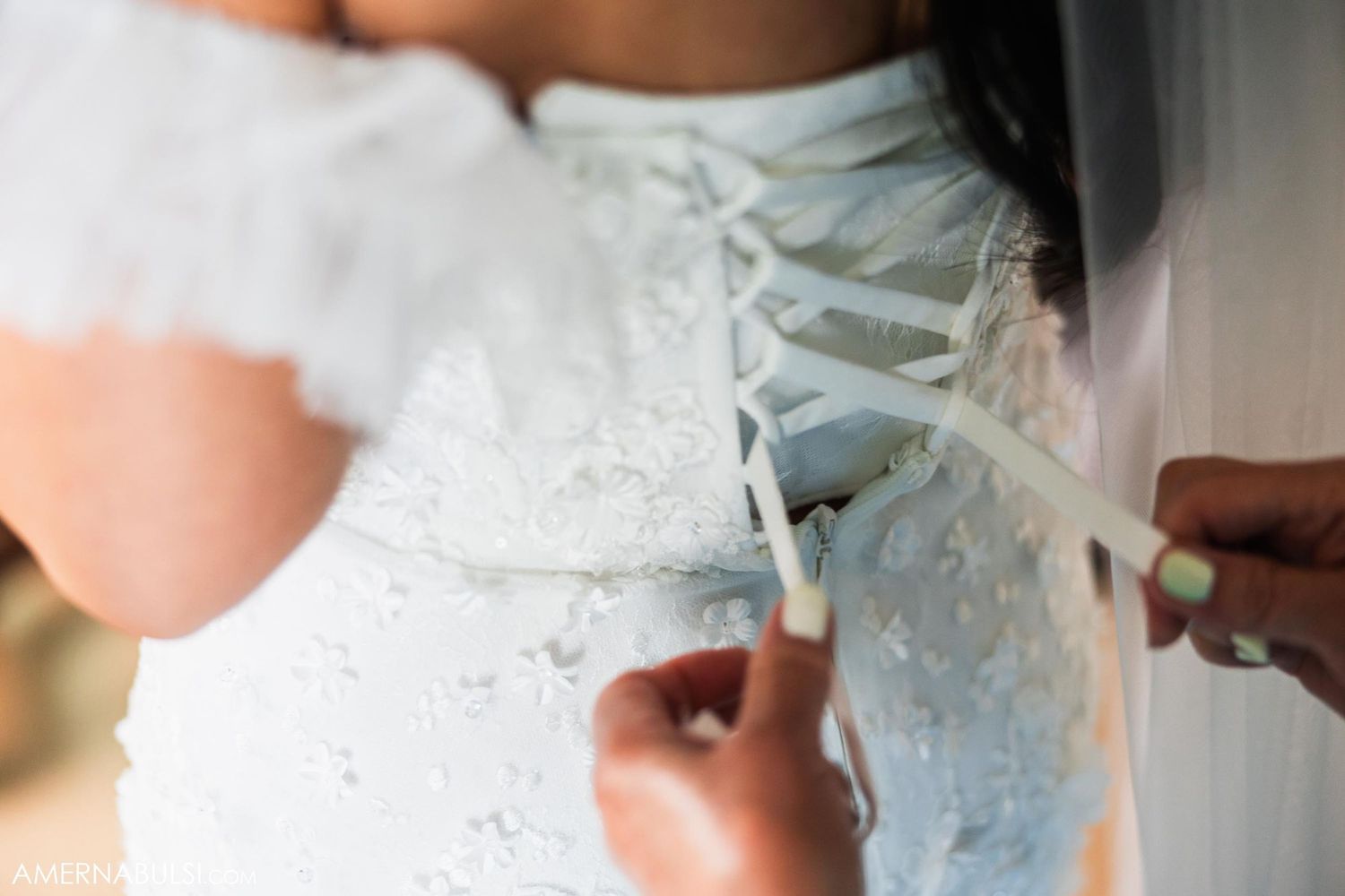 Close-up detail of white wedding dress being laced up in corset style.