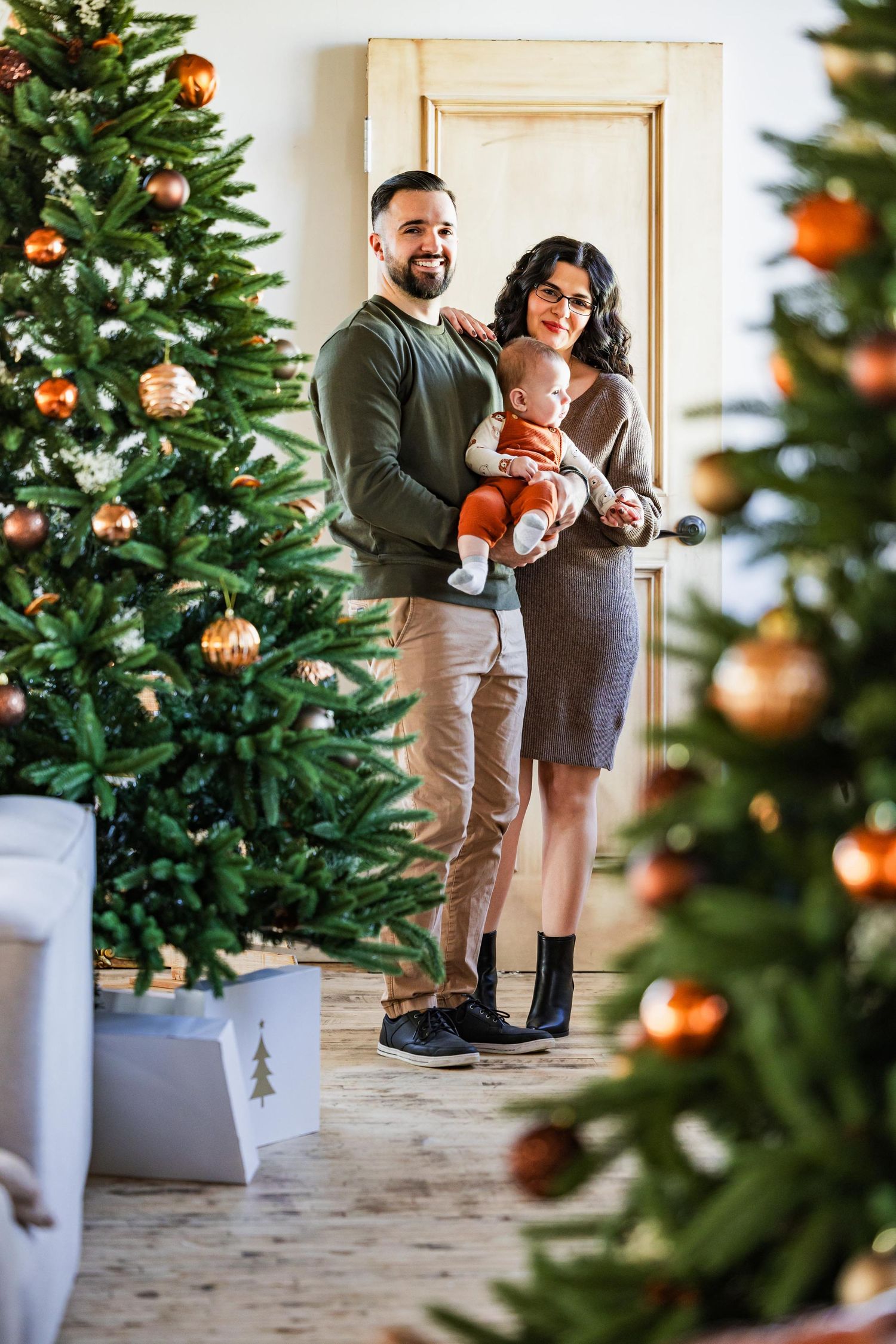 A family poses together by decorated Christmas trees in a bright interior setting.