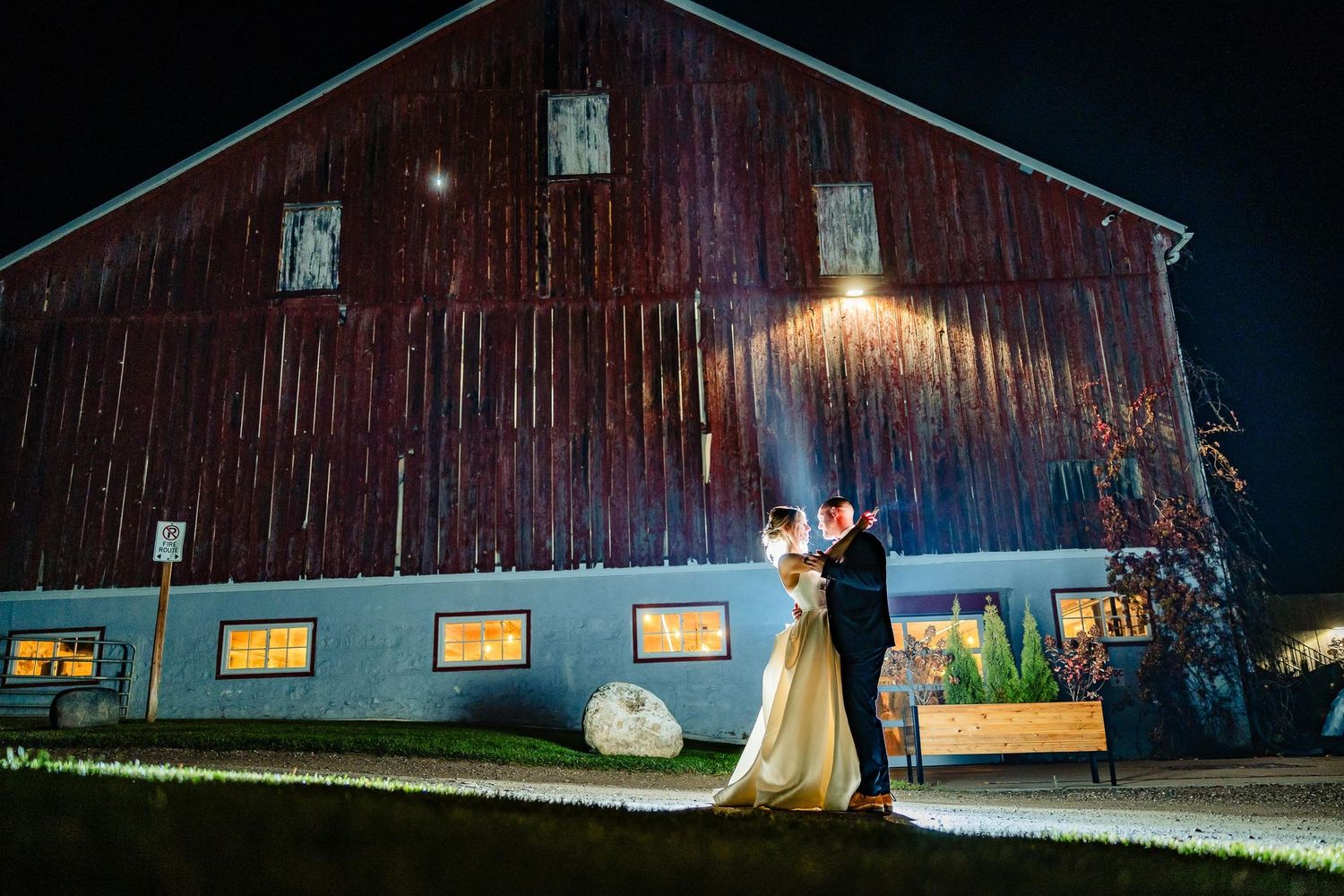 A couple shares an intimate moment outside a rustic barn illuminated at night.