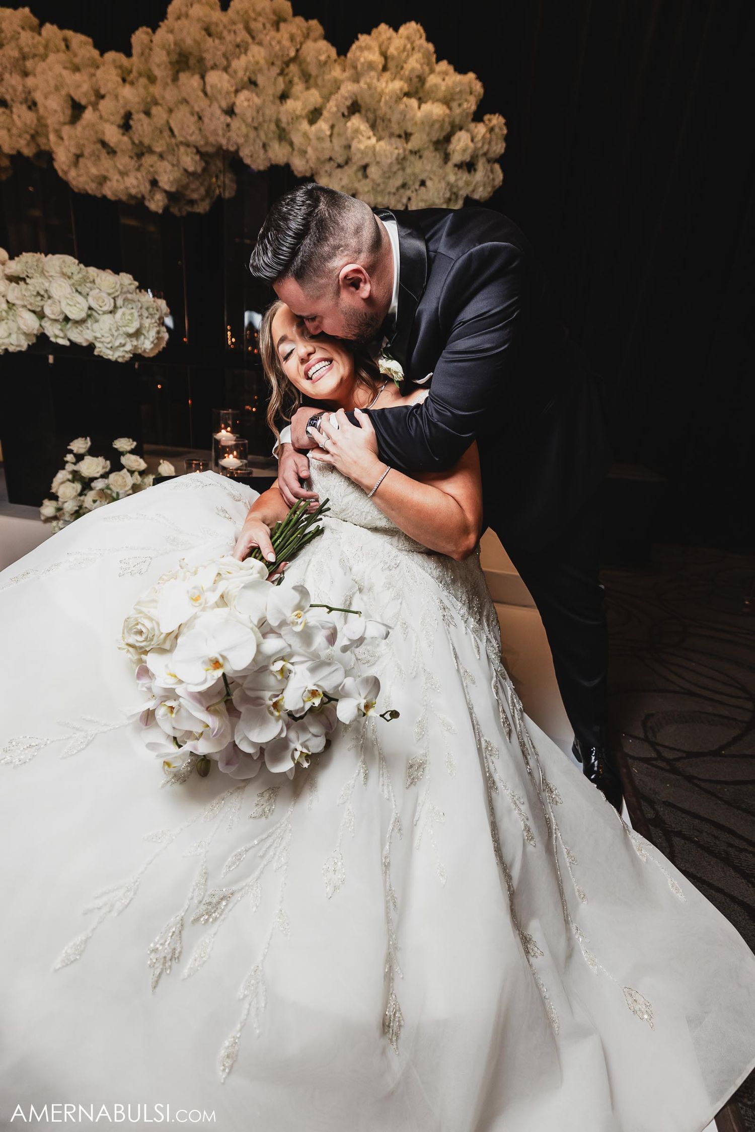 Intimate wedding moment captured with dramatic lighting and floral backdrop.