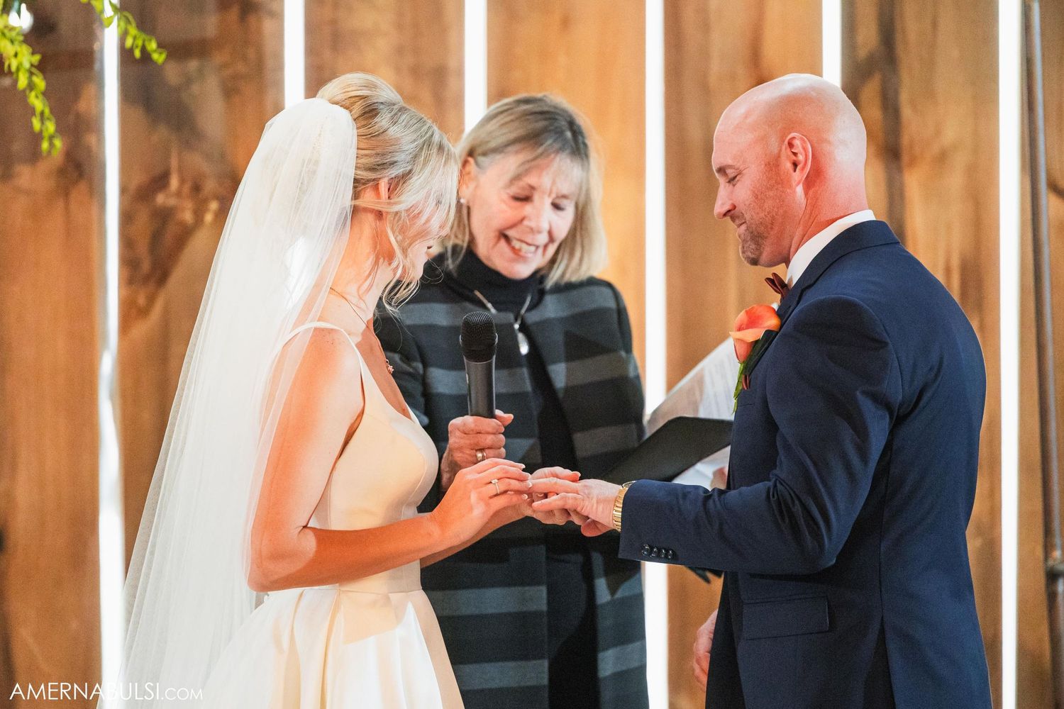 Exchange of rings during barn wedding ceremony with officiant in striped dress.