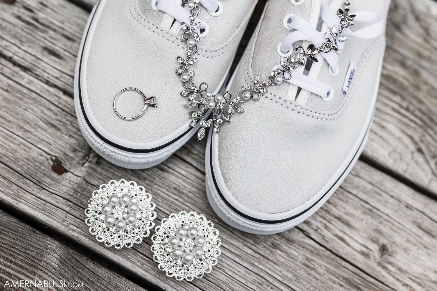 White sneakers with wedding rings and crystal jewelry arranged on wooden deck for wedding detail photo.