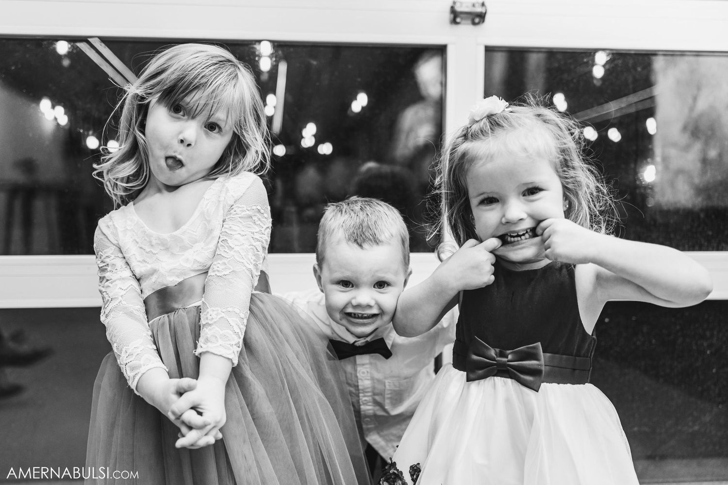 Three young children dressed in formal attire laughing and making silly faces at a special event.