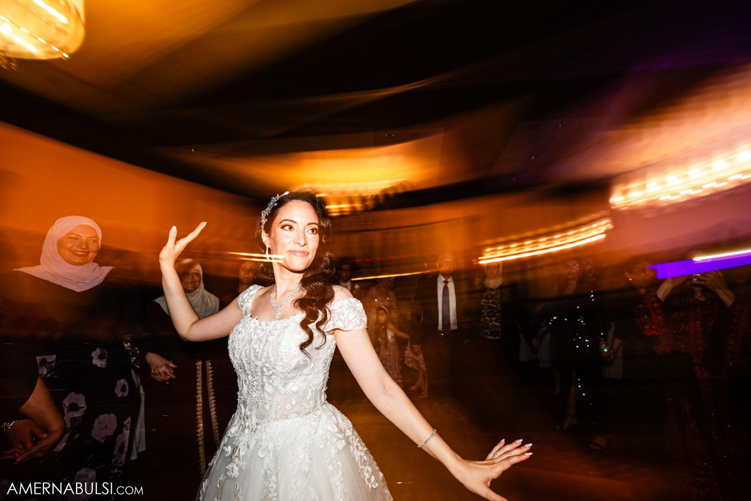 A bride in a white gown dances gracefully under golden ambient lighting at her wedding reception.
