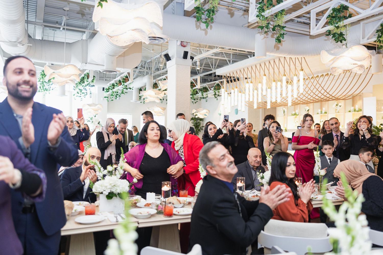 Wedding reception guests applauding during a celebration in a light-filled modern venue.