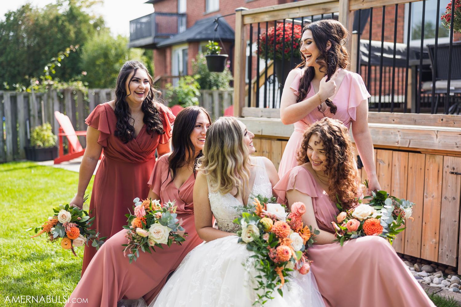 Wedding party in coordinated dusty rose dresses gathered on outdoor deck with bouquets.