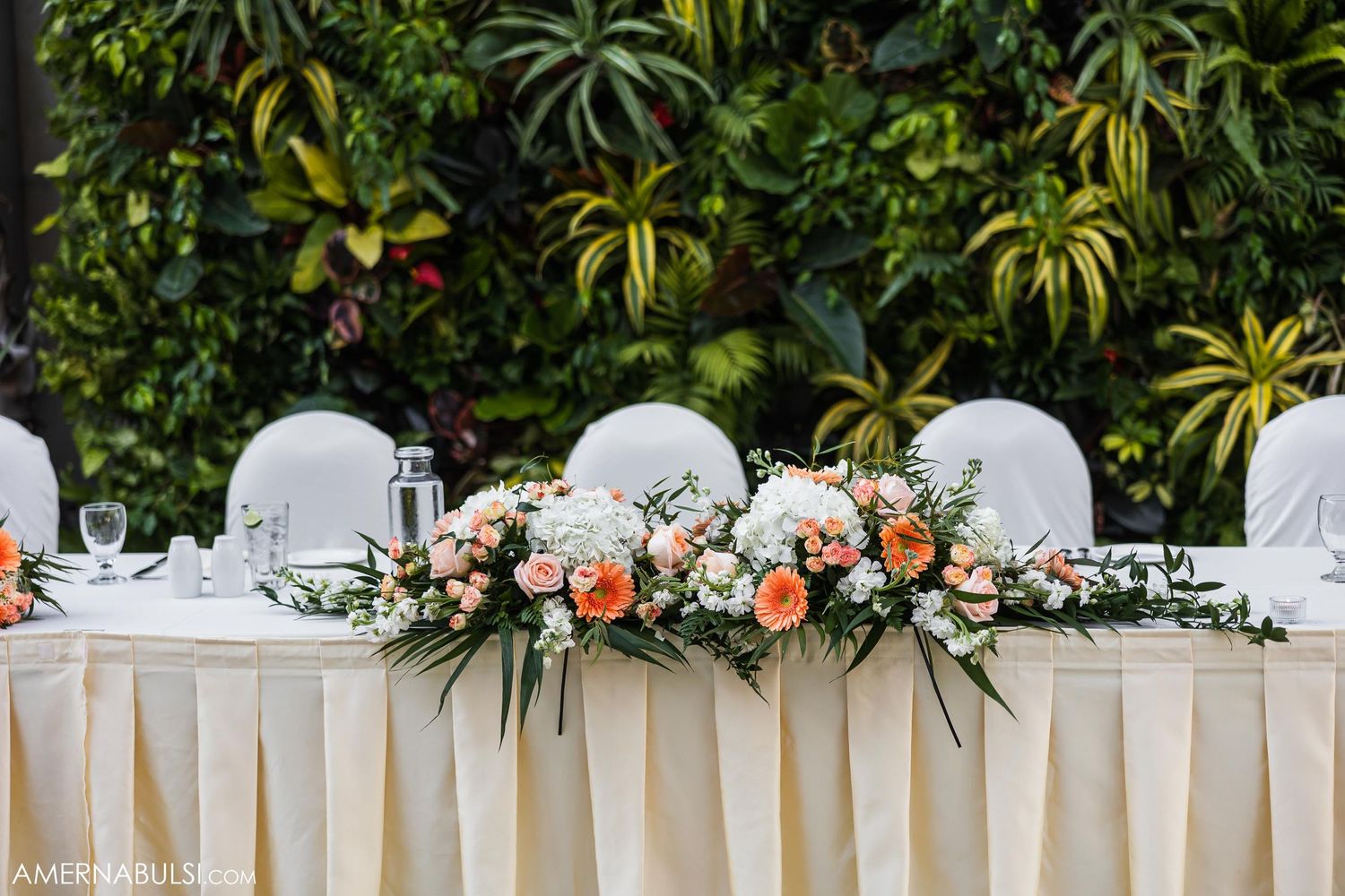 Elegant wedding head table decorated with white and peach floral arrangements and draped linens.
