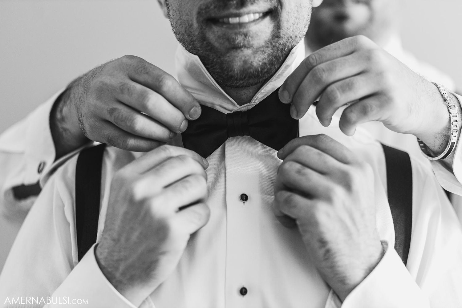 Black and white photo showing hands adjusting a bow tie with formal shirt.