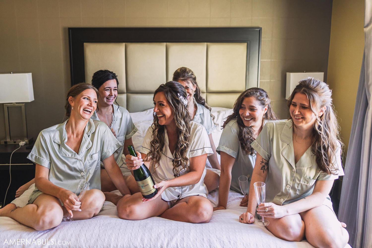 Group enjoying champagne while sitting on bed in matching pajama sets.