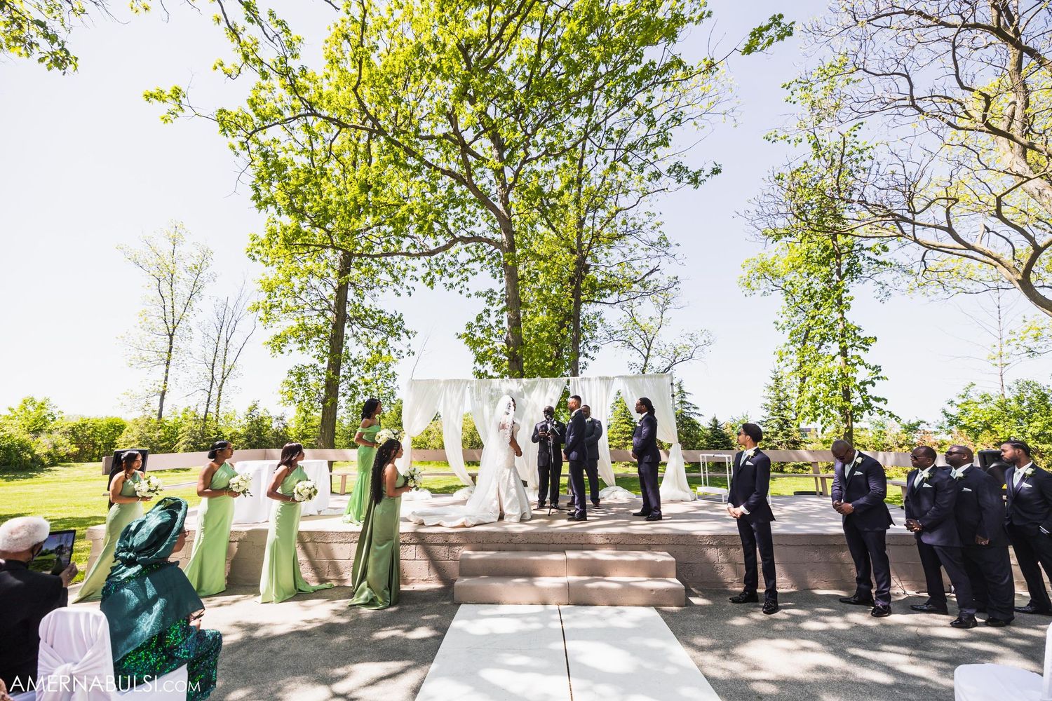 Wide shot of outdoor wedding ceremony setup with white altar and guests on both sides.