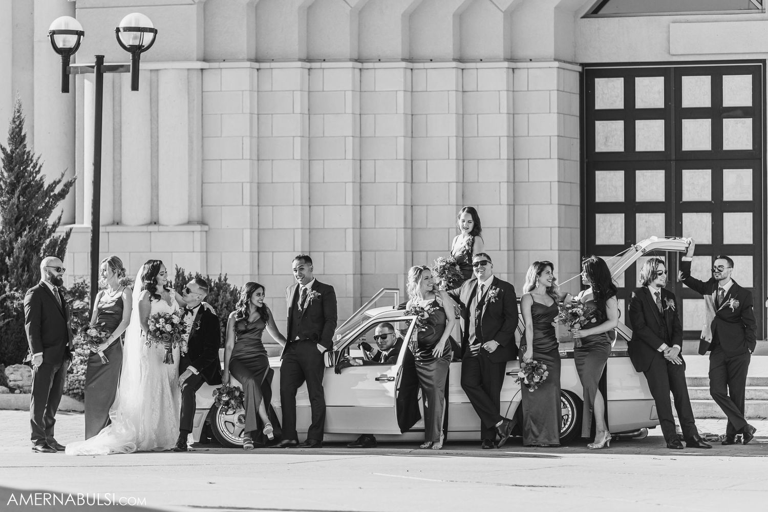 Wedding party poses outdoors against modern architectural backdrop with dramatic lighting.