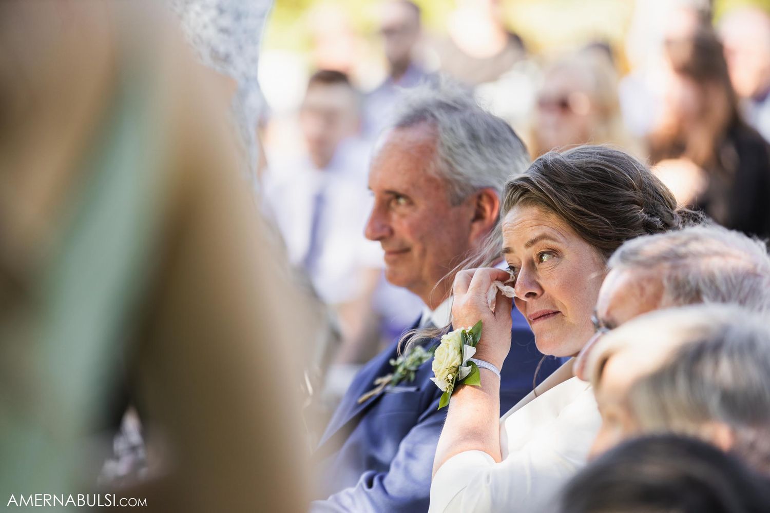 Wedding guests watch the ceremony with emotional expressions while seated outdoors.
