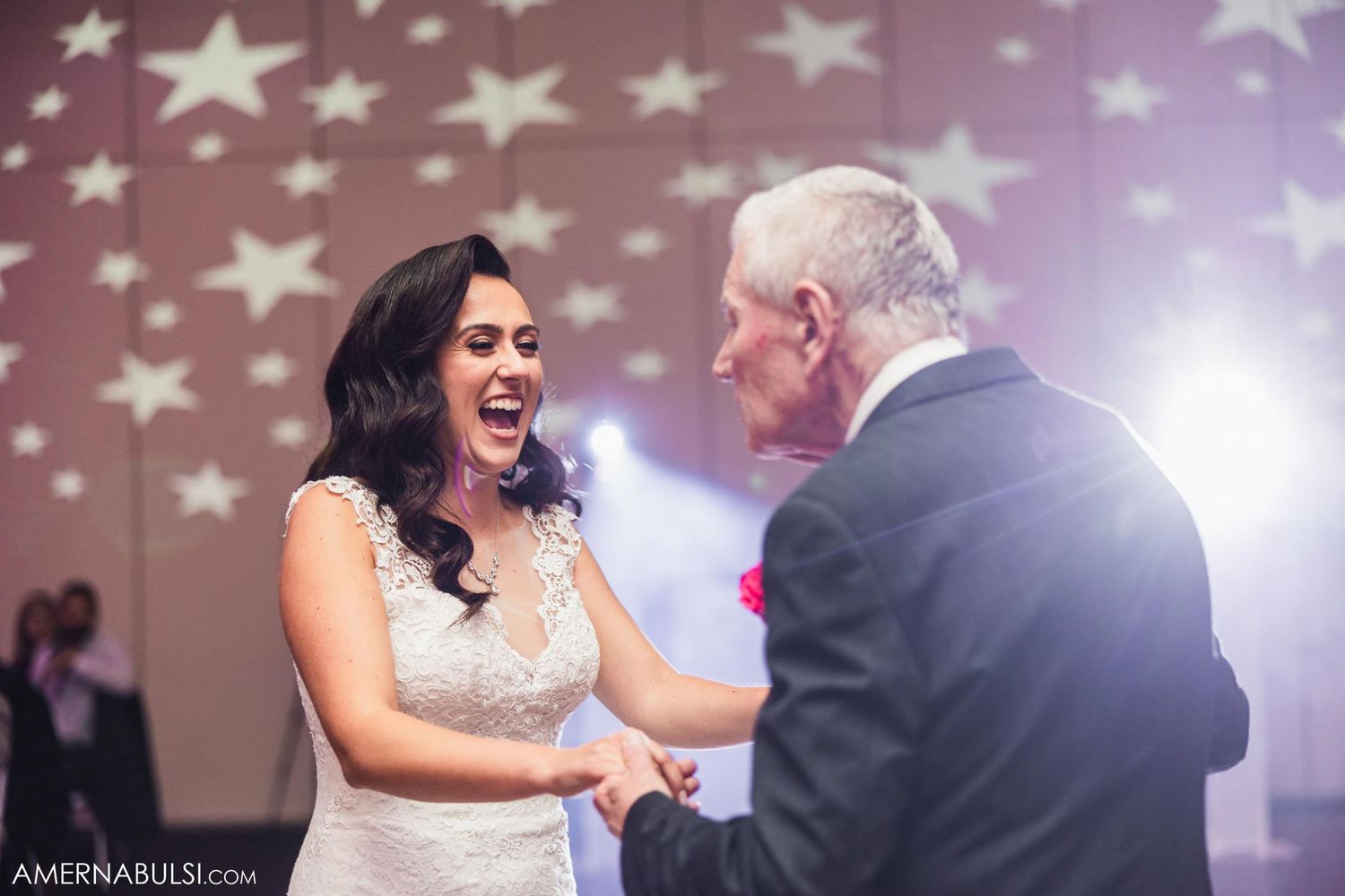Bride sharing joyful moment with partner during dance under projected star patterns.
