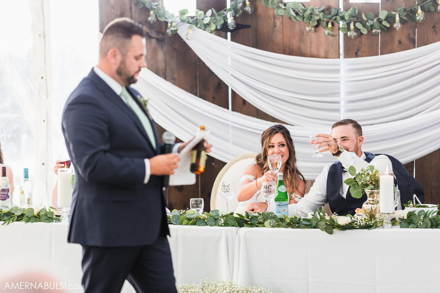 Wedding speech moment during reception with decorated white backdrop.