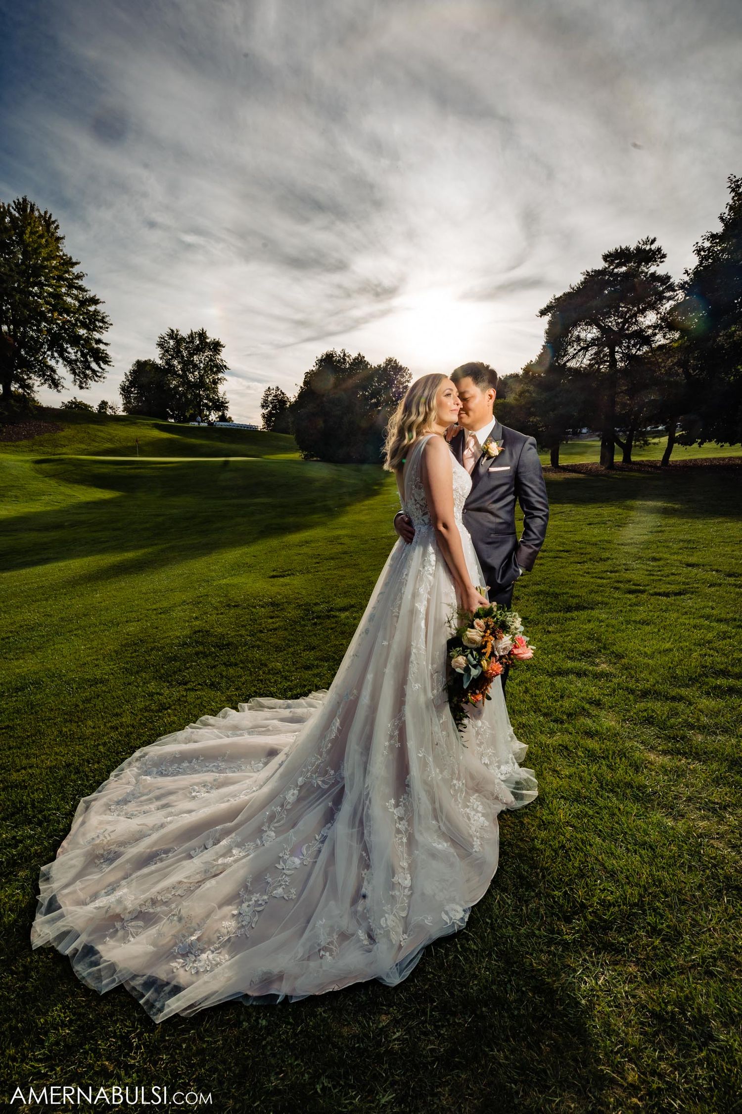 Dramatic sunset wedding portrait of couple on golf course with flowing bridal gown train.
