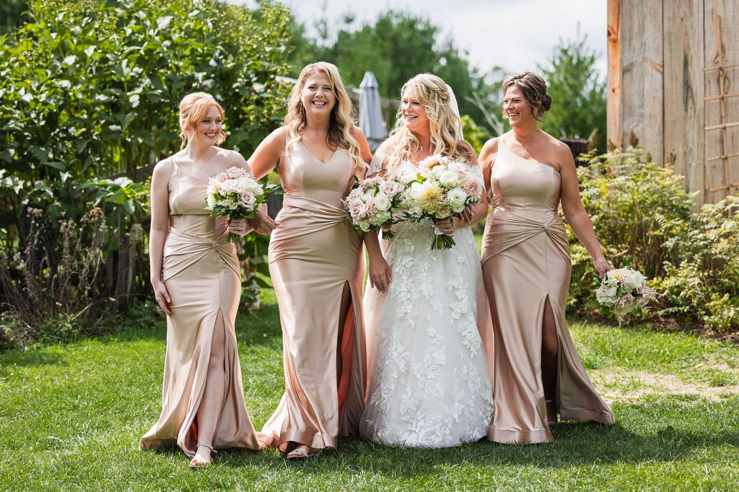 Bridesmaids in champagne-colored dresses pose with flowers in a garden setting.