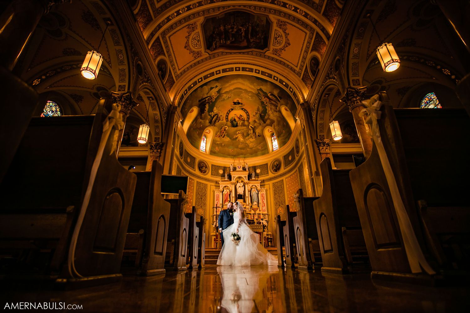 Wedding ceremony in ornate cathedral with dramatic golden lighting and vaulted architectural details.