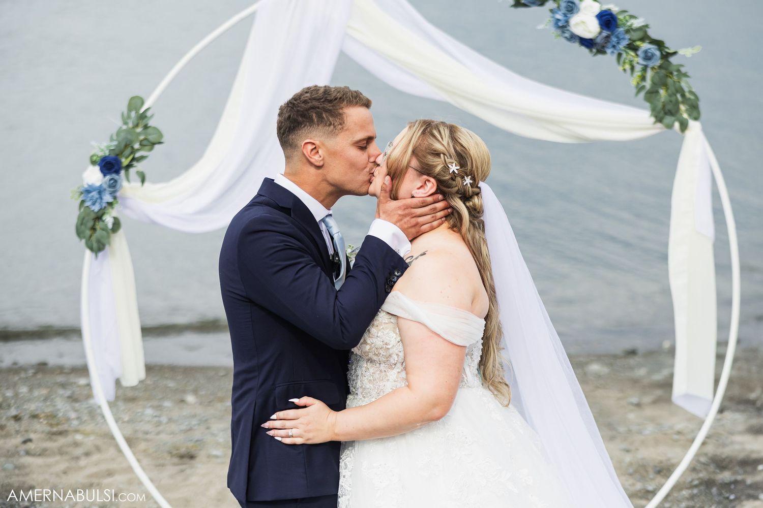 Beach wedding ceremony setup with white flowing fabric arch and ocean backdrop.