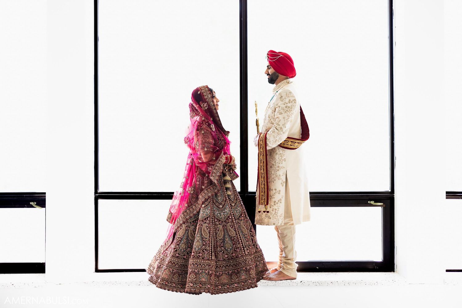 Minimalist portrait of a couple in traditional Indian wedding attire against a white backdrop.