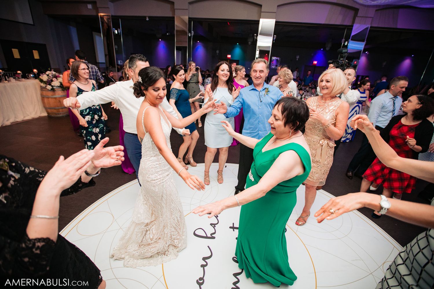 Wedding guests dancing and celebrating on a purple-lit dance floor at a reception party.