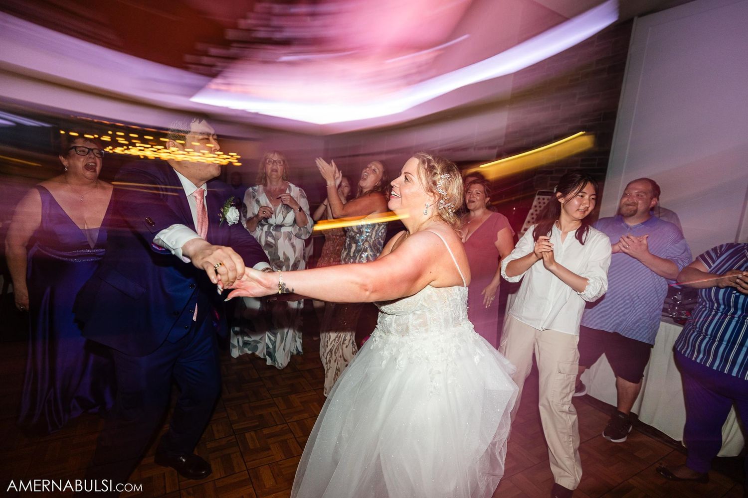 Wedding reception dance floor scene illuminated with pink and purple lighting.