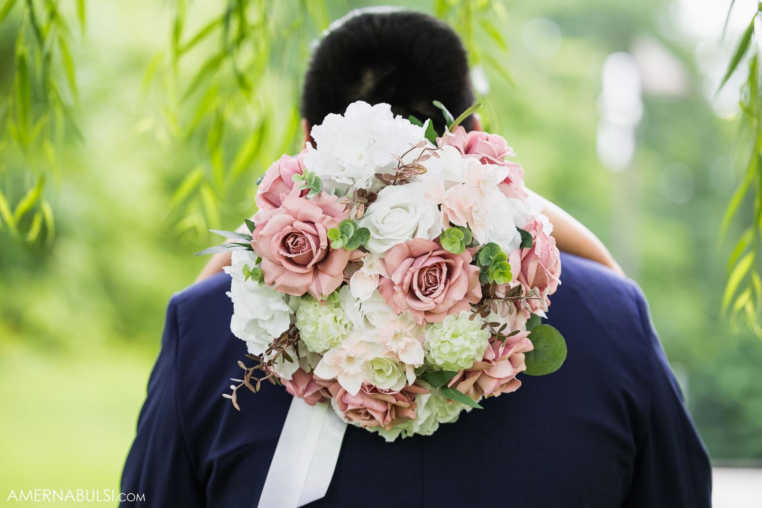A beautiful bridal bouquet with pink roses and white flowers against a navy suit and green foliage background.