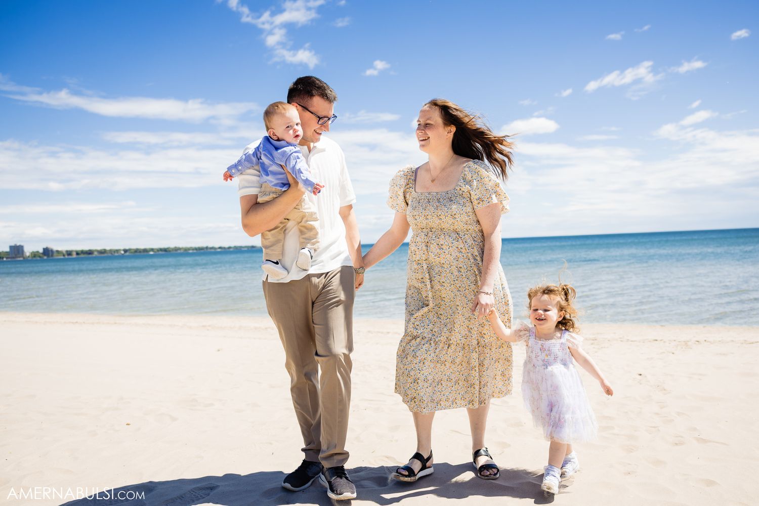 A family walks together on a sunny beach with turquoise water and blue skies in the background.