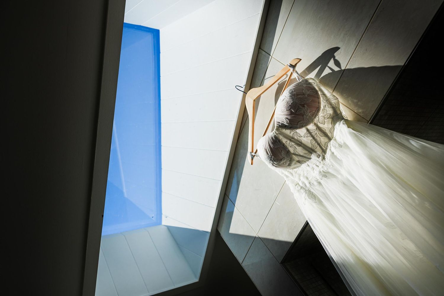 White wedding dress hanging in window with dramatic lighting and shadows.