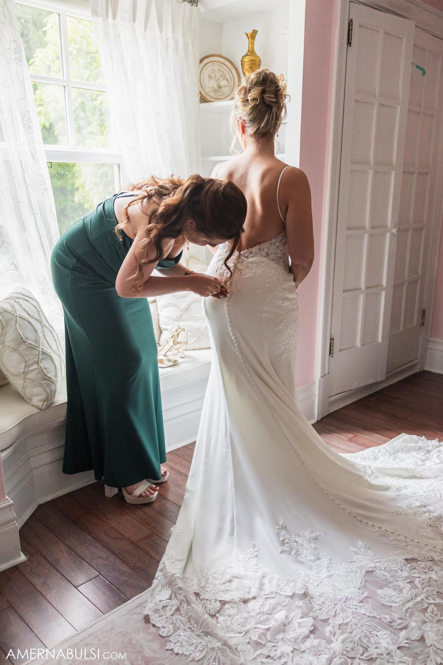 Helper assisting with final adjustments to a flowing white wedding gown.