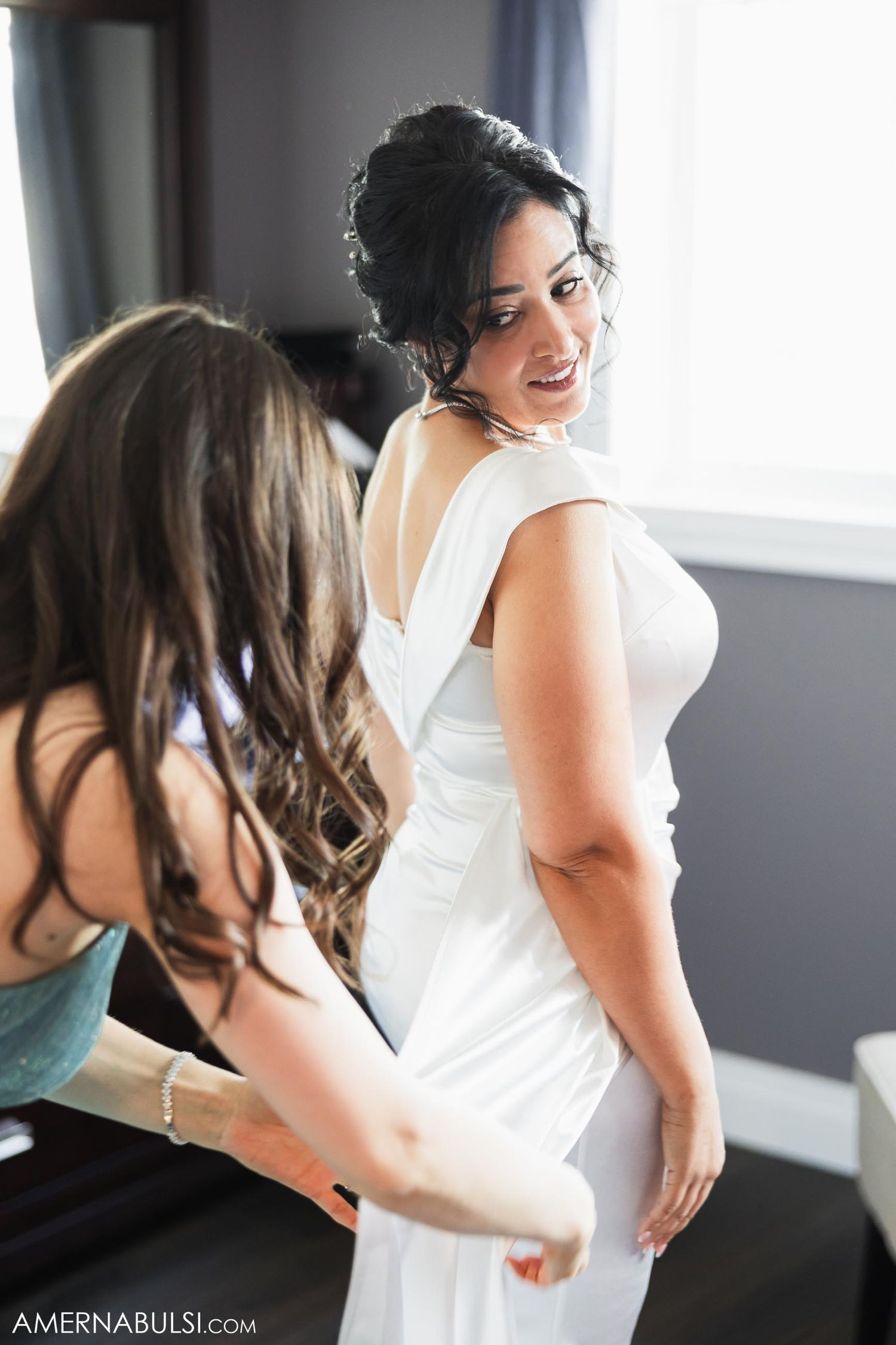Wedding dress being adjusted during final preparations by a window.