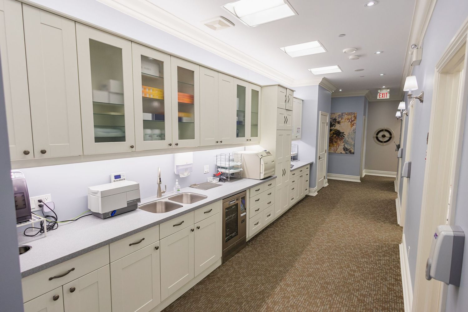 Modern dental office hallway with white cabinetry, built-in sink, and medical equipment along a carpeted corridor.