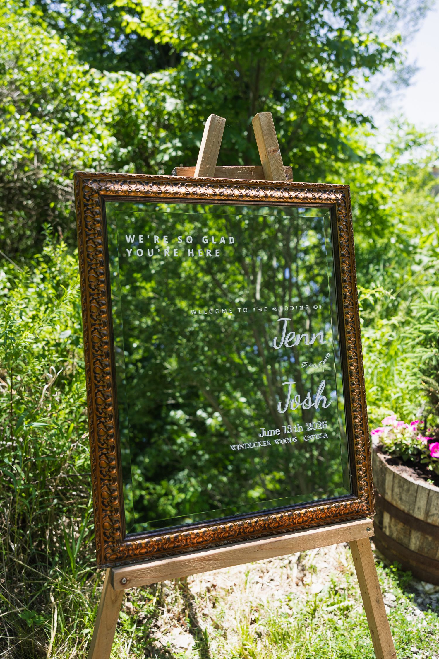 Elegant gold-framed mirror wedding welcome sign on wooden easel displaying Jenni and Josh's wedding date outdoors.