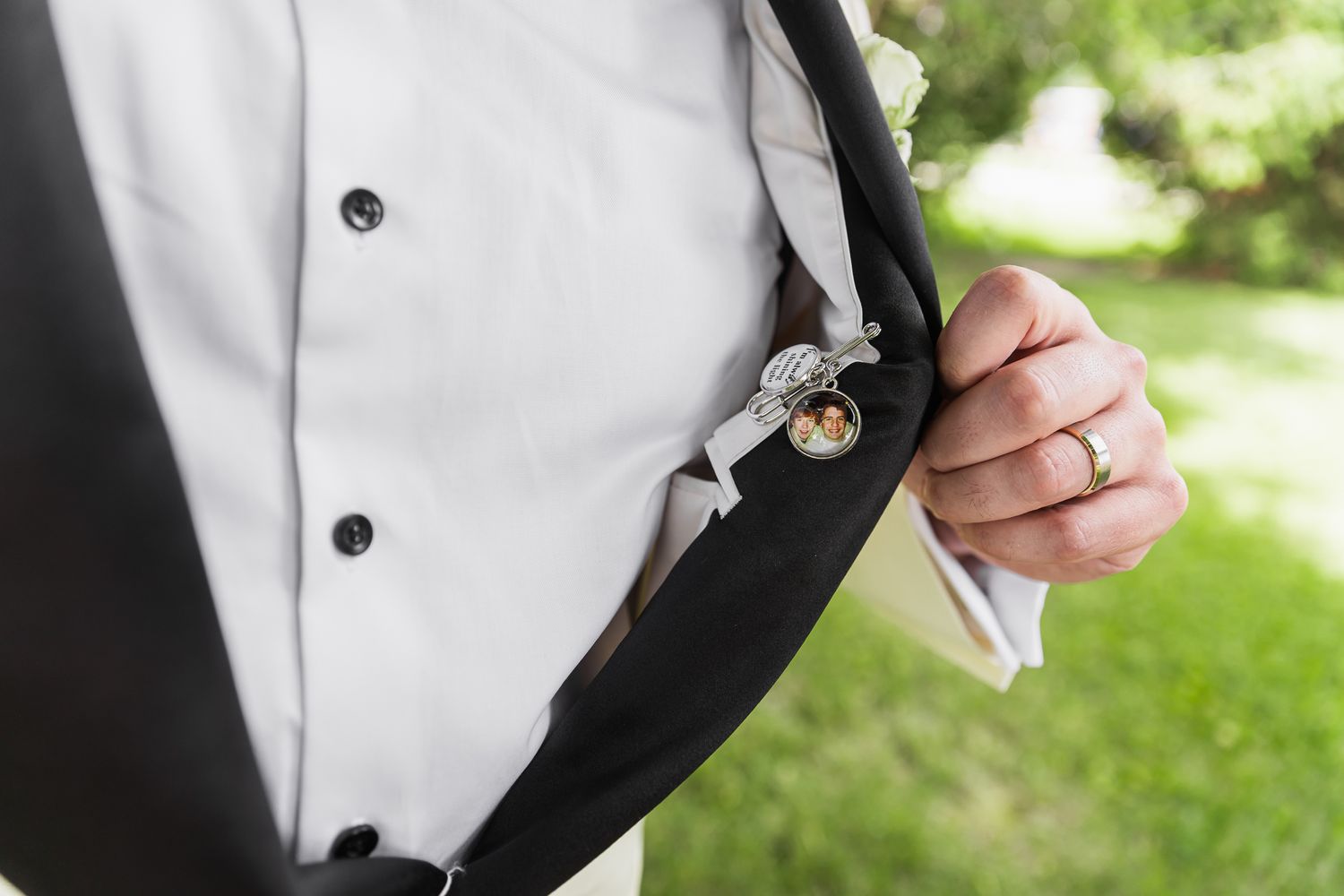 Groom in tuxedo displaying a pocket watch in his jacket pocket, wearing a gold wedding band.