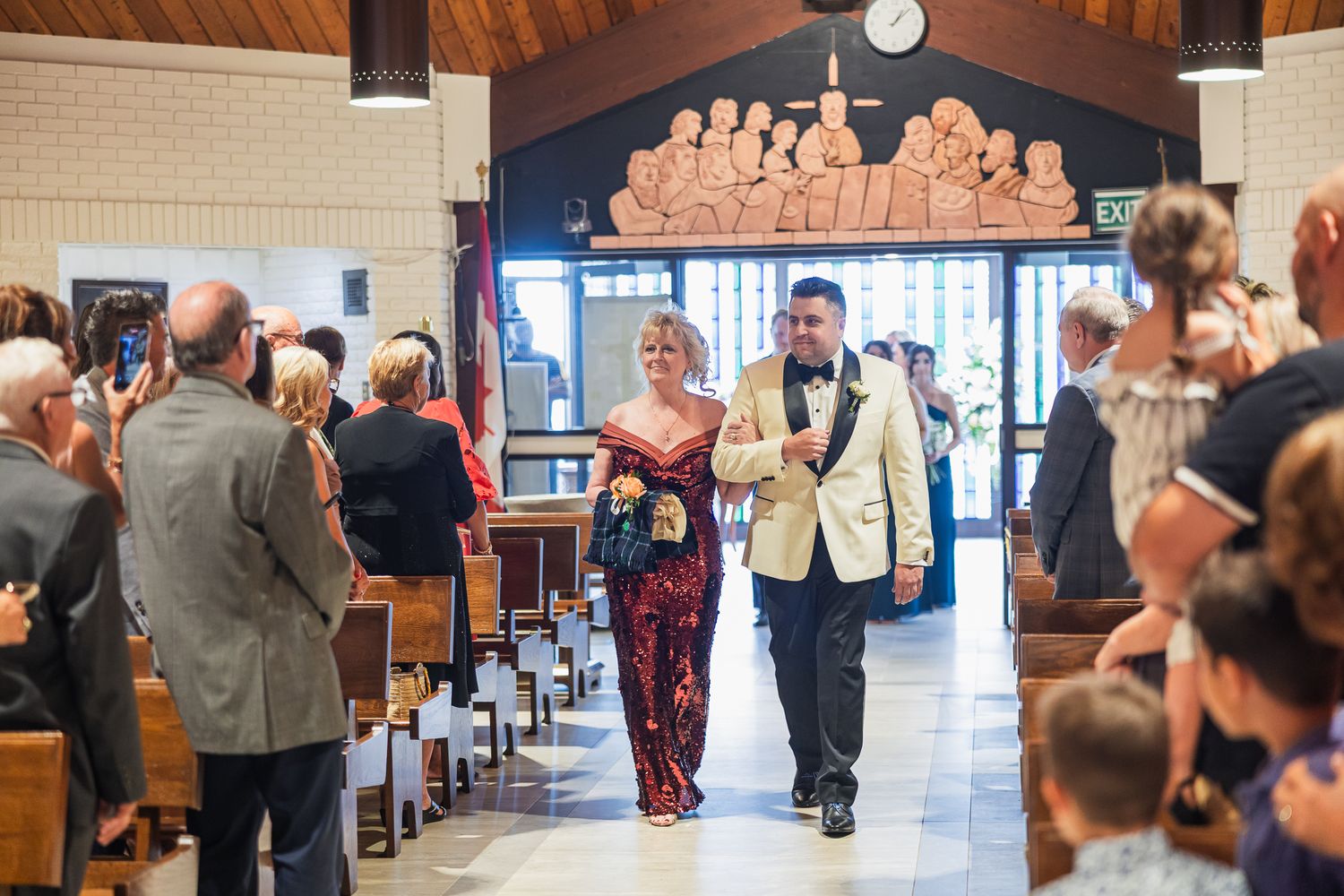 Groom in ivory tuxedo escorts a woman in a red gown down the church aisle.