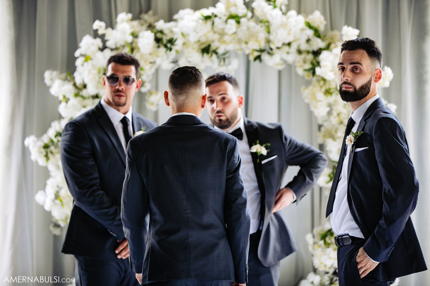 Wedding party members in black suits react with excitement and joy during an emotional moment at a ceremony.