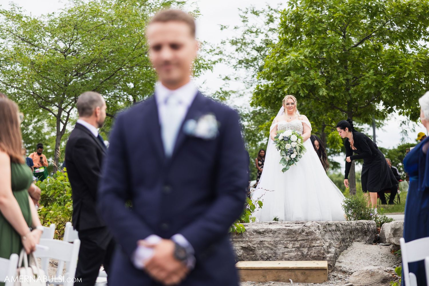 Outdoor wedding celebration with guests mingling near stone walls and lush greenery.
