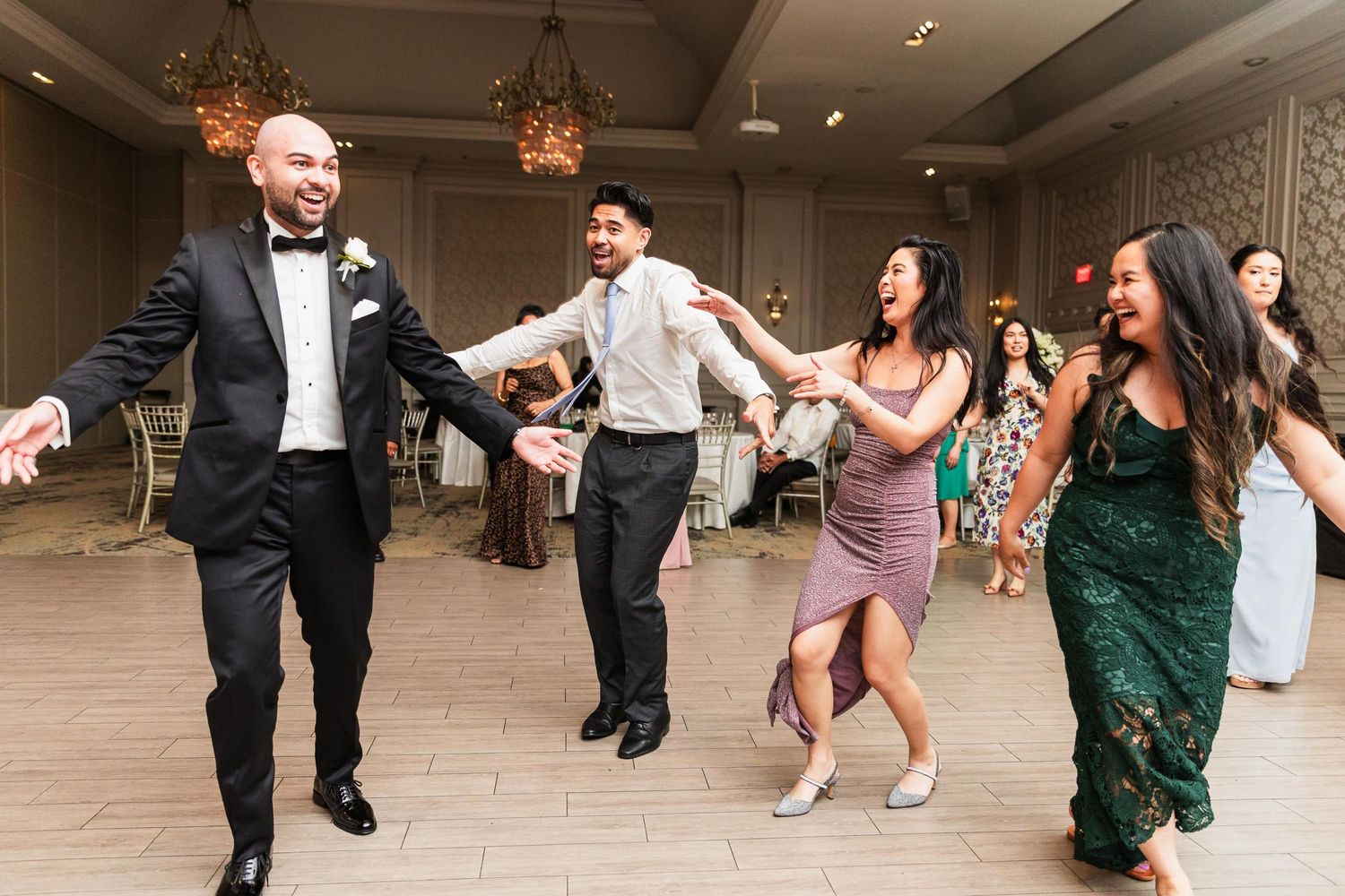 Wedding guests dance in formal attire on a reception dance floor.