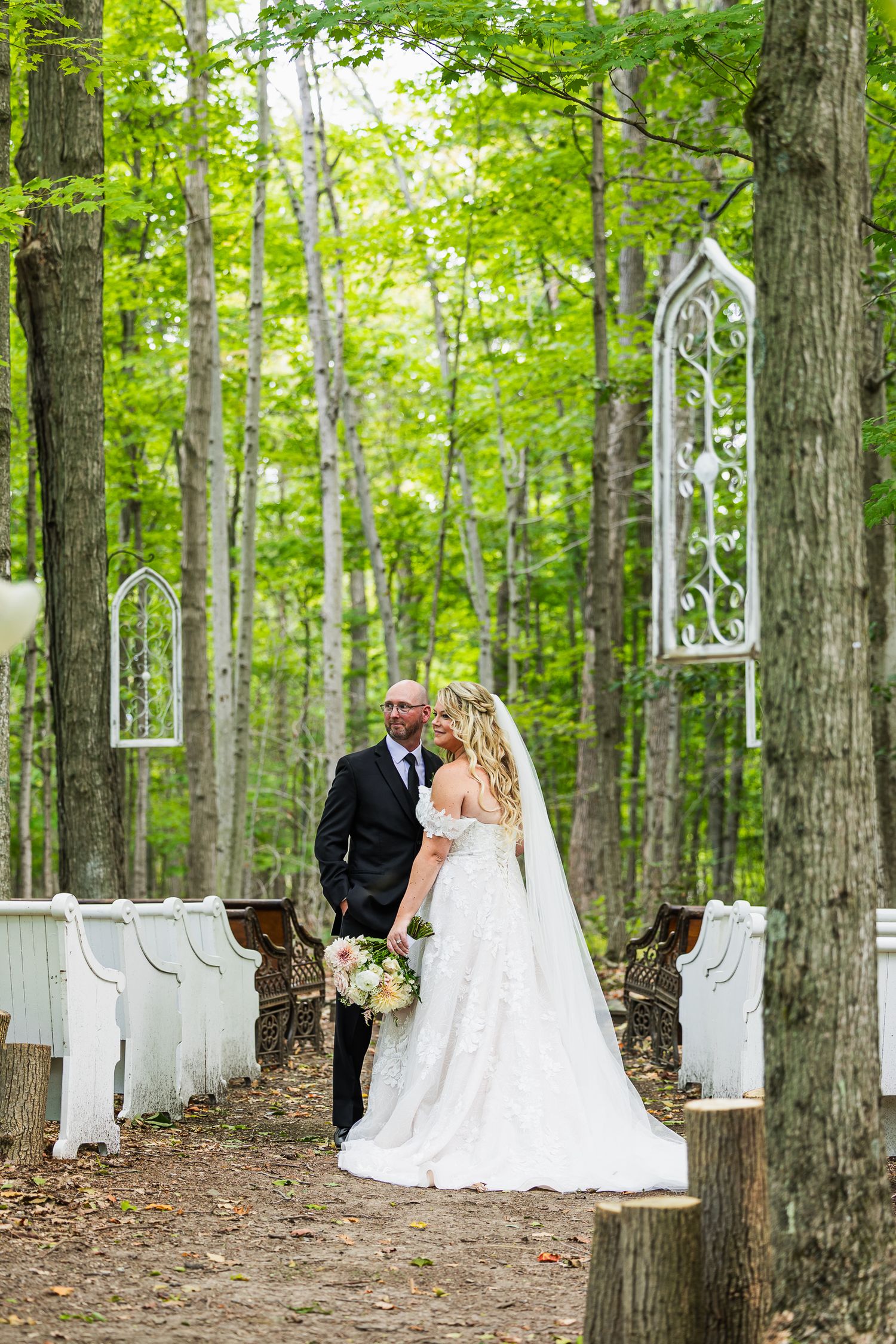 White chairs line a forest path creating a romantic woodland wedding ceremony setting with ethereal window frames.