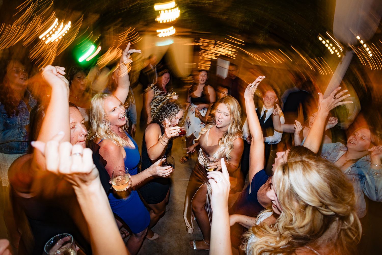 Energetic dance floor scene at a wedding reception with colorful lighting effects.