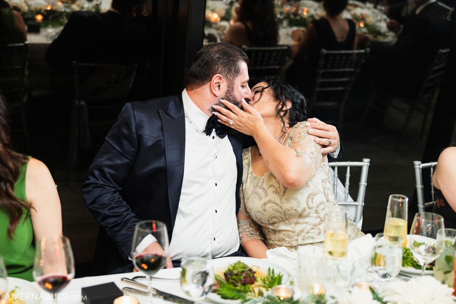 Romantic moment between newlyweds sharing a kiss at their reception dinner table.