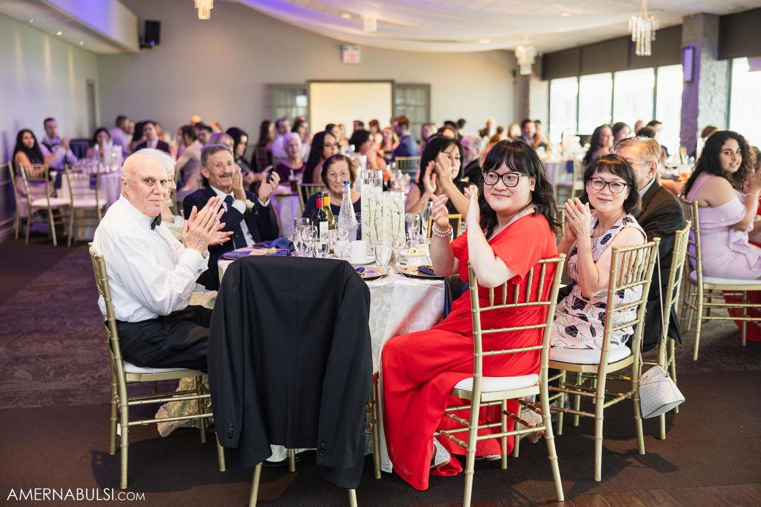 Wedding reception guests seated at decorated tables with purple uplighting in an elegant venue.