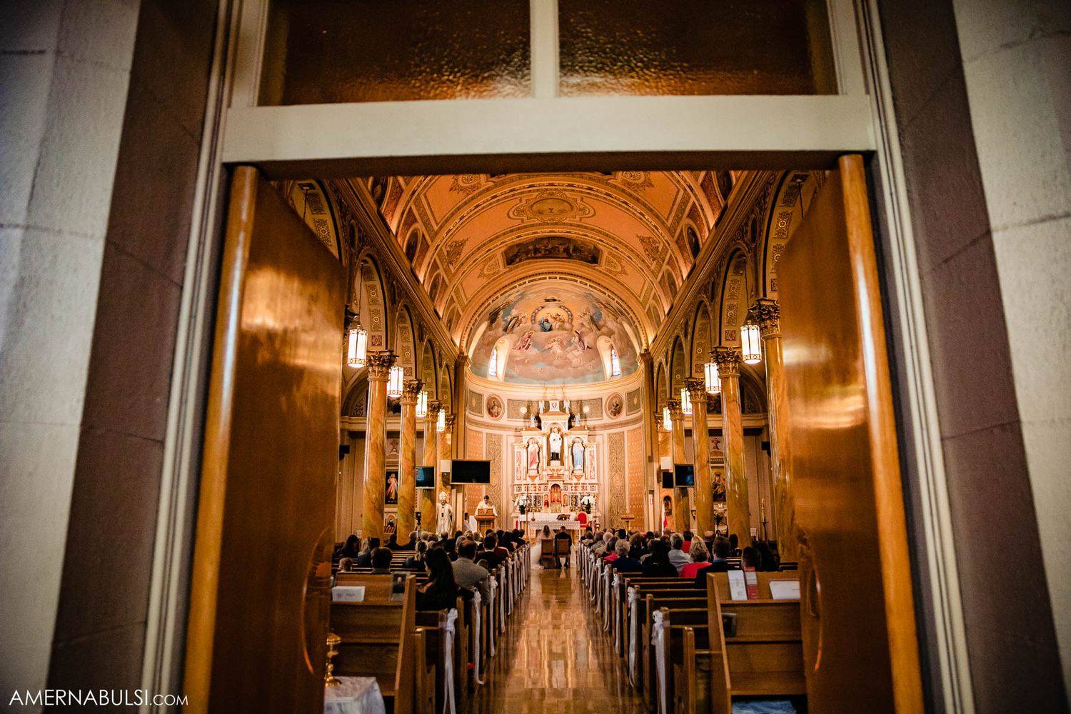 Interior view of a grand church during a wedding ceremony with warm lighting and arched ceilings.